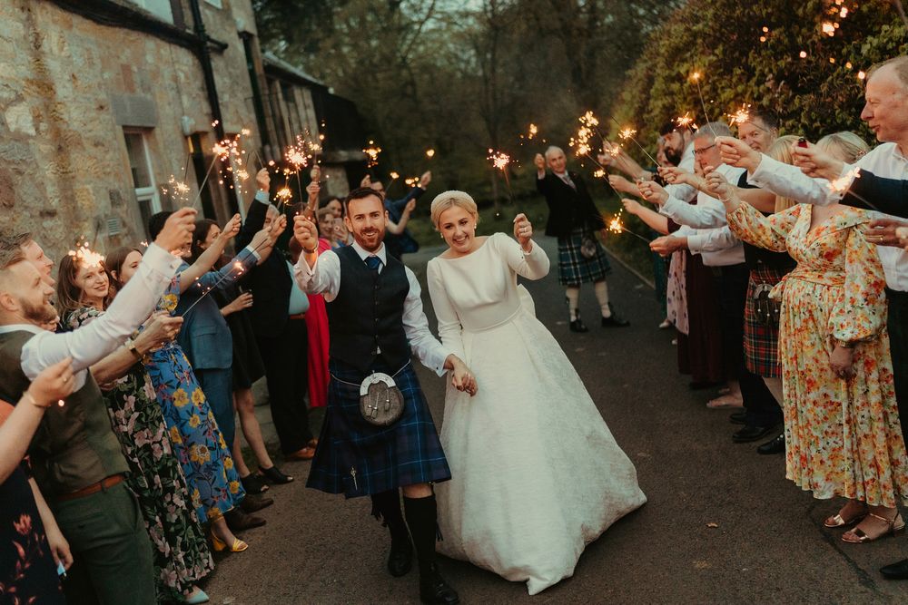 Guests line a pathway with sparklers as newlyweds walk through in celebration at a Scottish wedding.