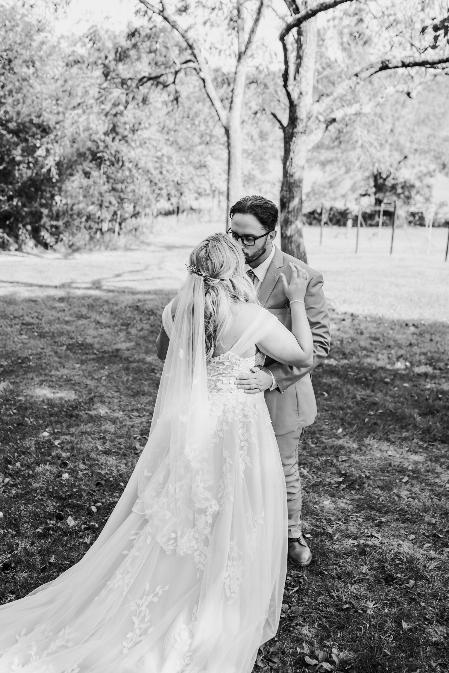 Black and white portrait of newlyweds embracing outdoors with flowing wedding veil.