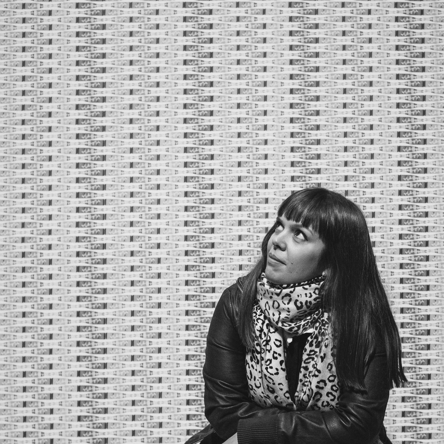 A black and white portrait against a geometric patterned wall background.