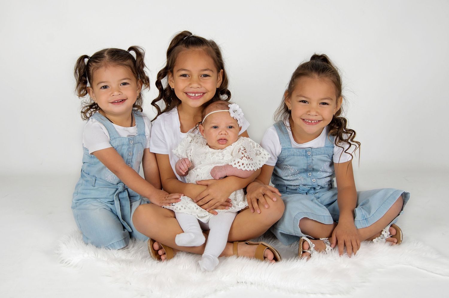 3 young girls holding baby sister smiling at camera in studio