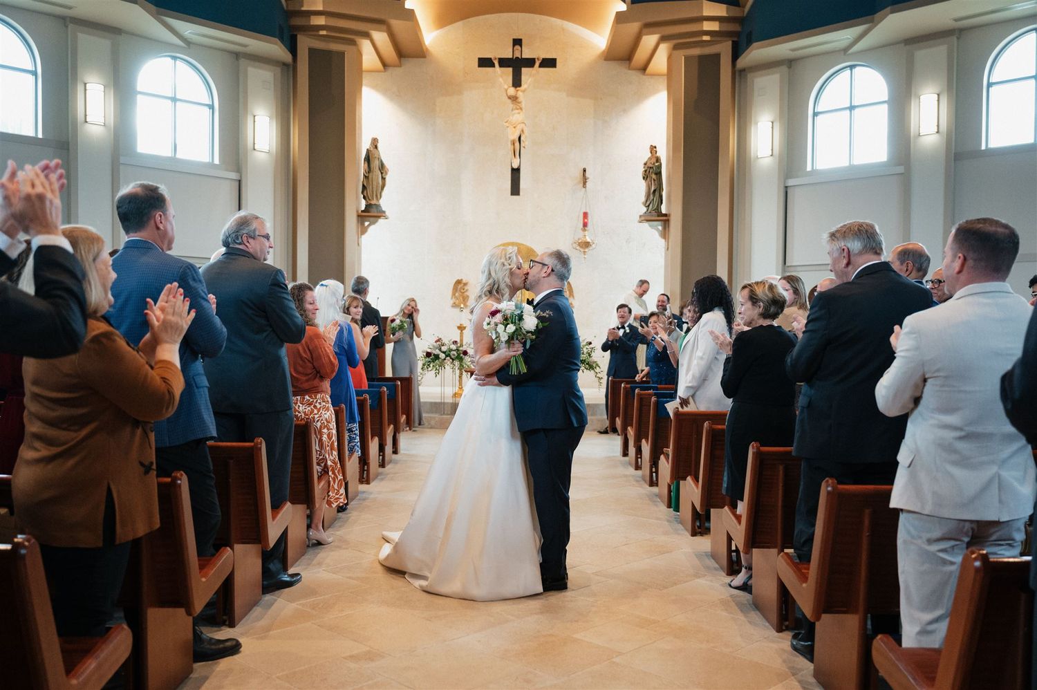Wedding guests applaud as the couple exits down the center aisle of a traditional church.