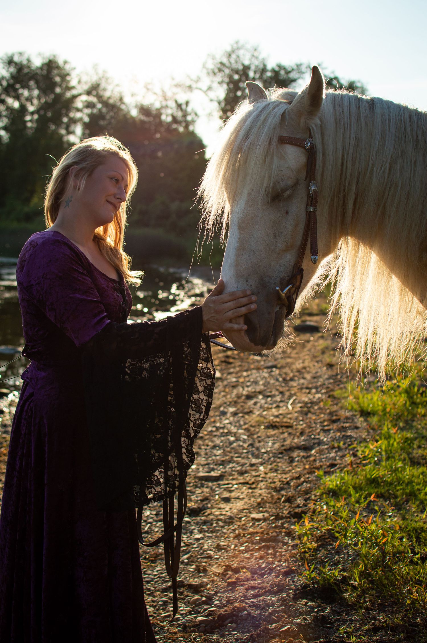 Woman in purple dress connecting with white horse during golden hour sunset.