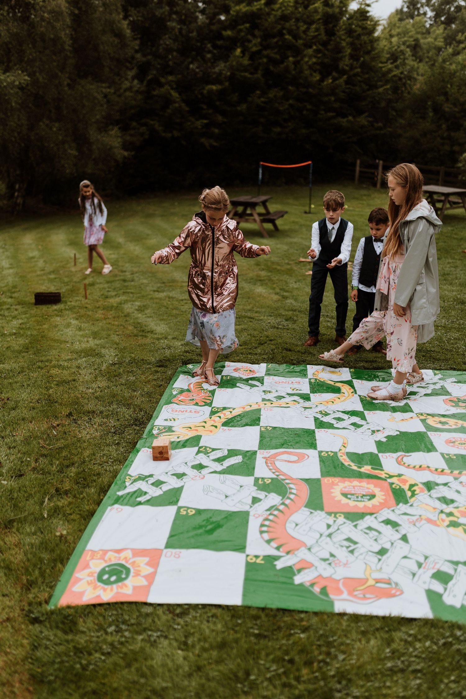Children playing giant snakes and ladders at wedding on lawn