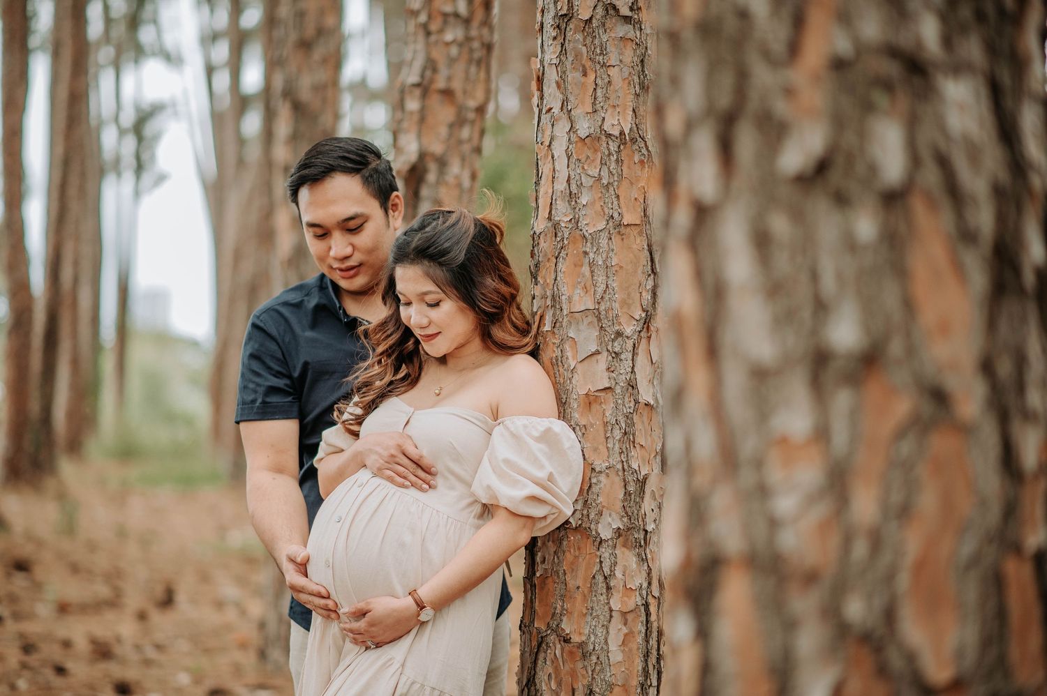 Intimate maternity photo of couple leaning against pine tree in forest.