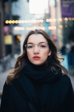 a portrait of a young woman in winter, in a black coat, with blurry lights at the background