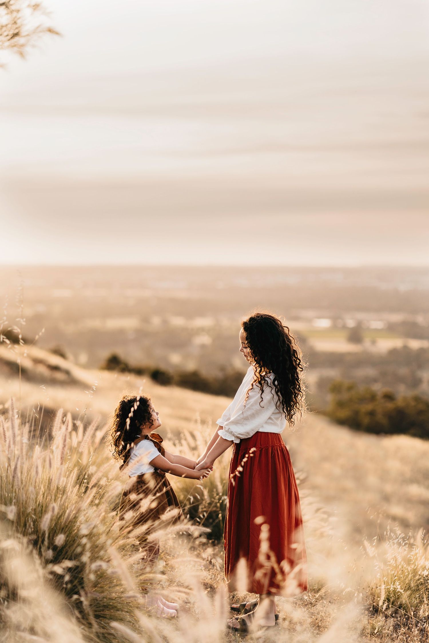 A mother and daughter sharing a sunset moment in a golden field overlooking a valley.