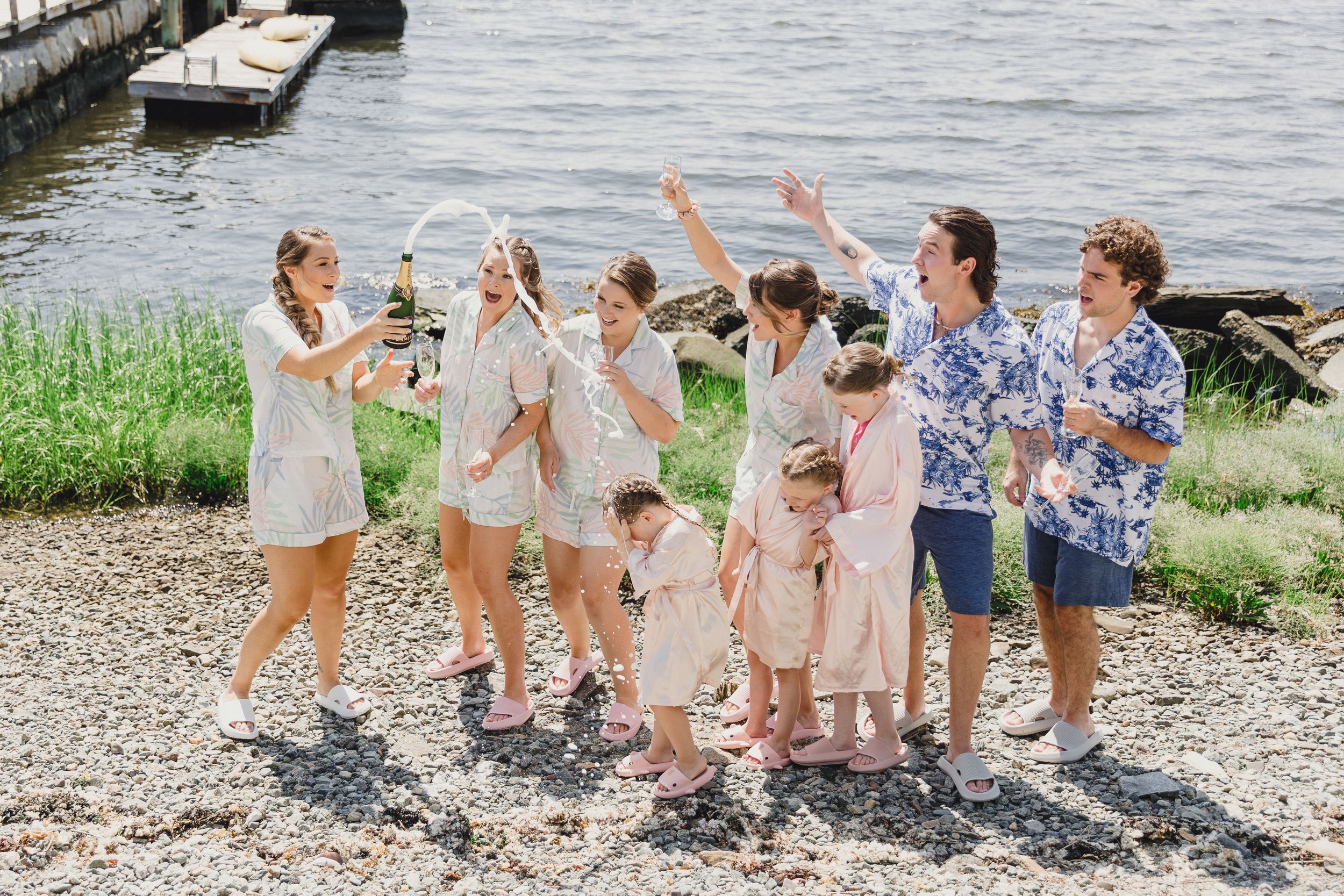 Group celebrates with champagne on a sunny waterfront with boats in background.