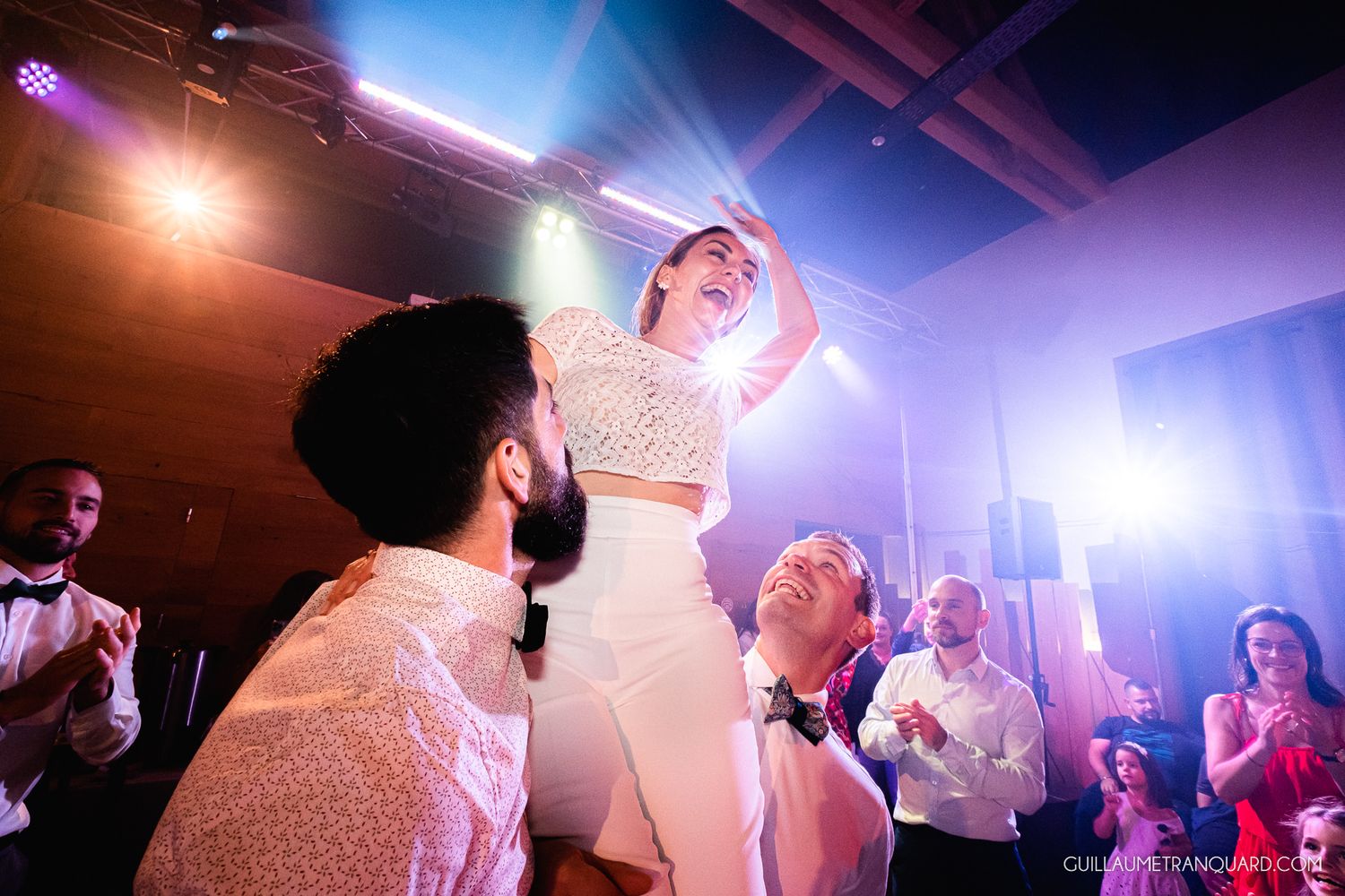 Vibrant purple and blue lighting illuminates a lively dance floor at an evening celebration.