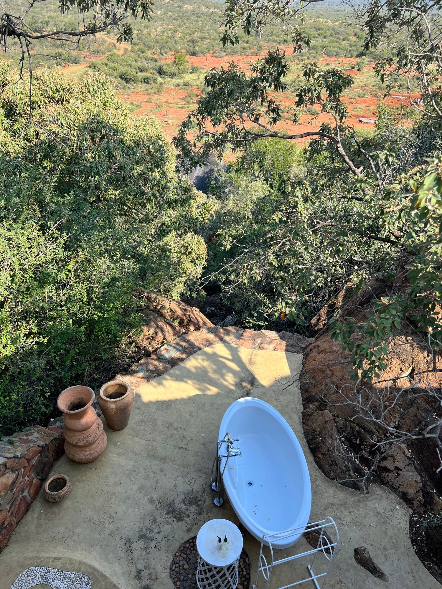 Outdoor terrace with clay pots and blue pool overlooking African bush landscape.