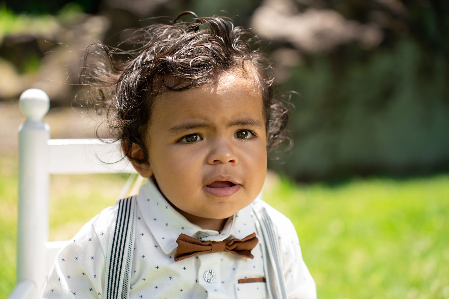 A small child in formal wear smiles while standing outdoors with balloons in the background.