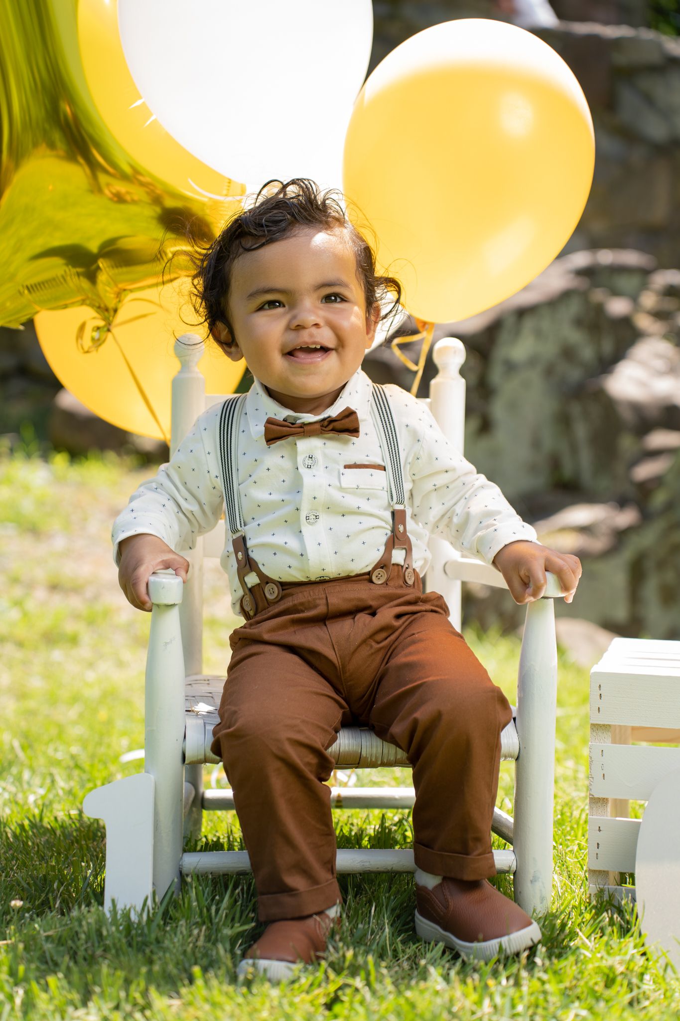 A small chair decorated with yellow balloons sits on green grass during a celebration.