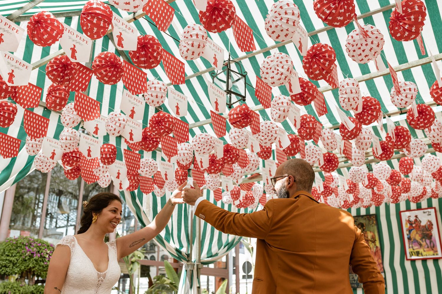Decorative red and white polka dot lanterns and green striped banners create a festive canopy overhead at an outdoor celebration in Seville