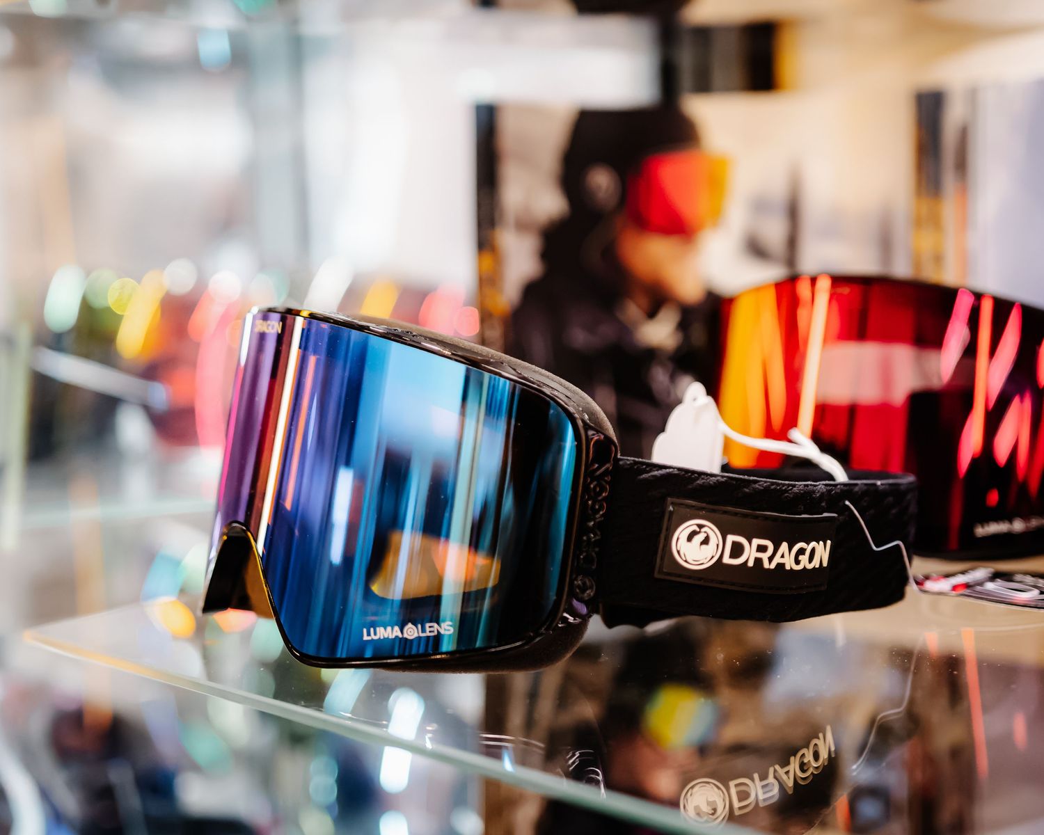 Dragon brand ski goggles with blue mirrored lens displayed on a glass shelf in a shop.