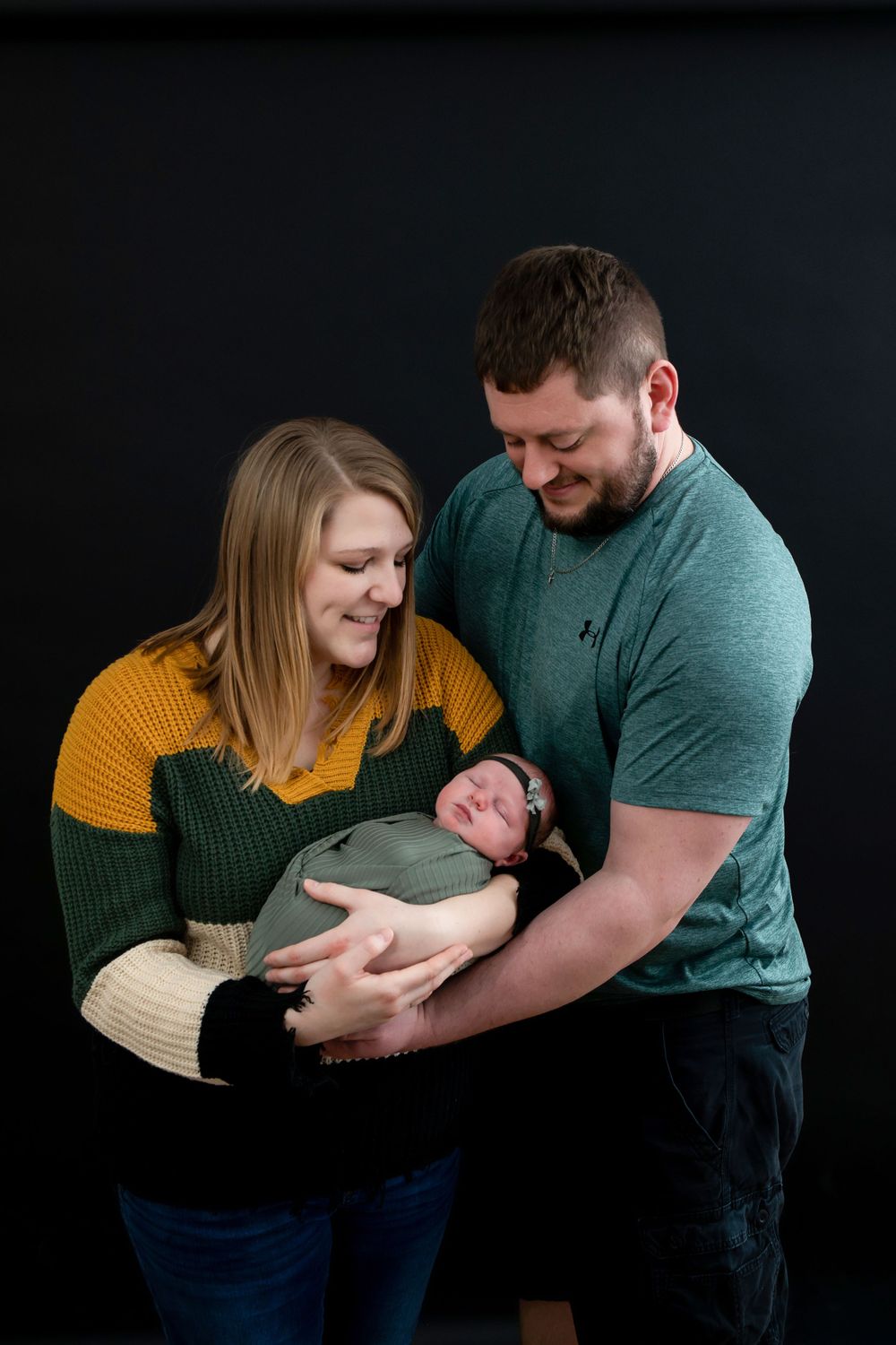 Family portrait against black background showing tender moment with newborn.
