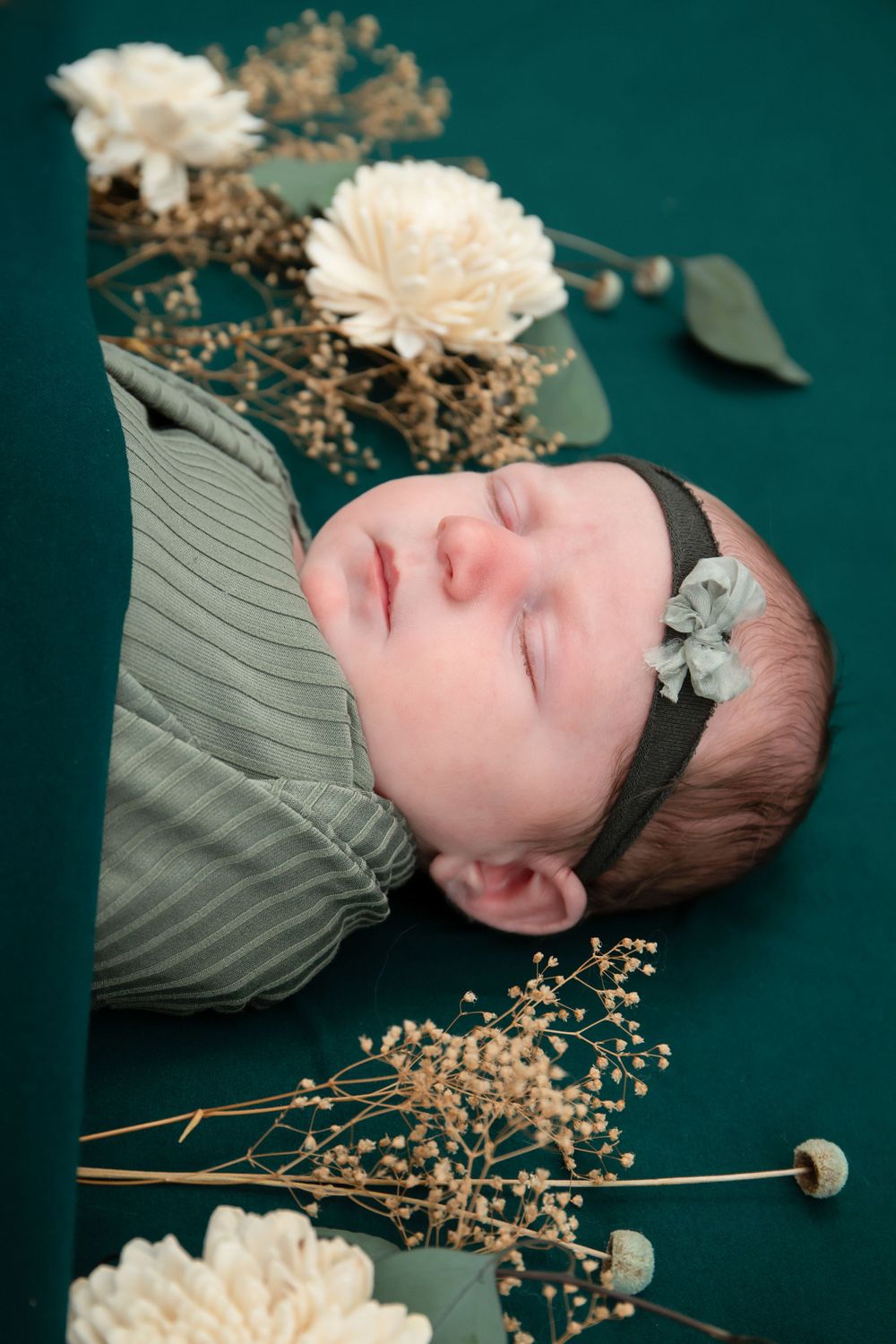 Baby sleeping on emerald background surrounded by white flowers and delicate dried floral accents.