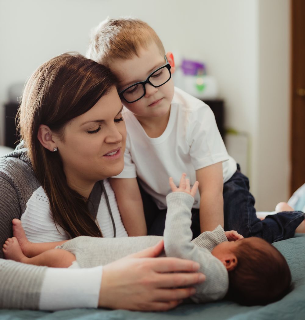 Indoor lifestyle newborn session with baby on bed surrounded by mom and big brother