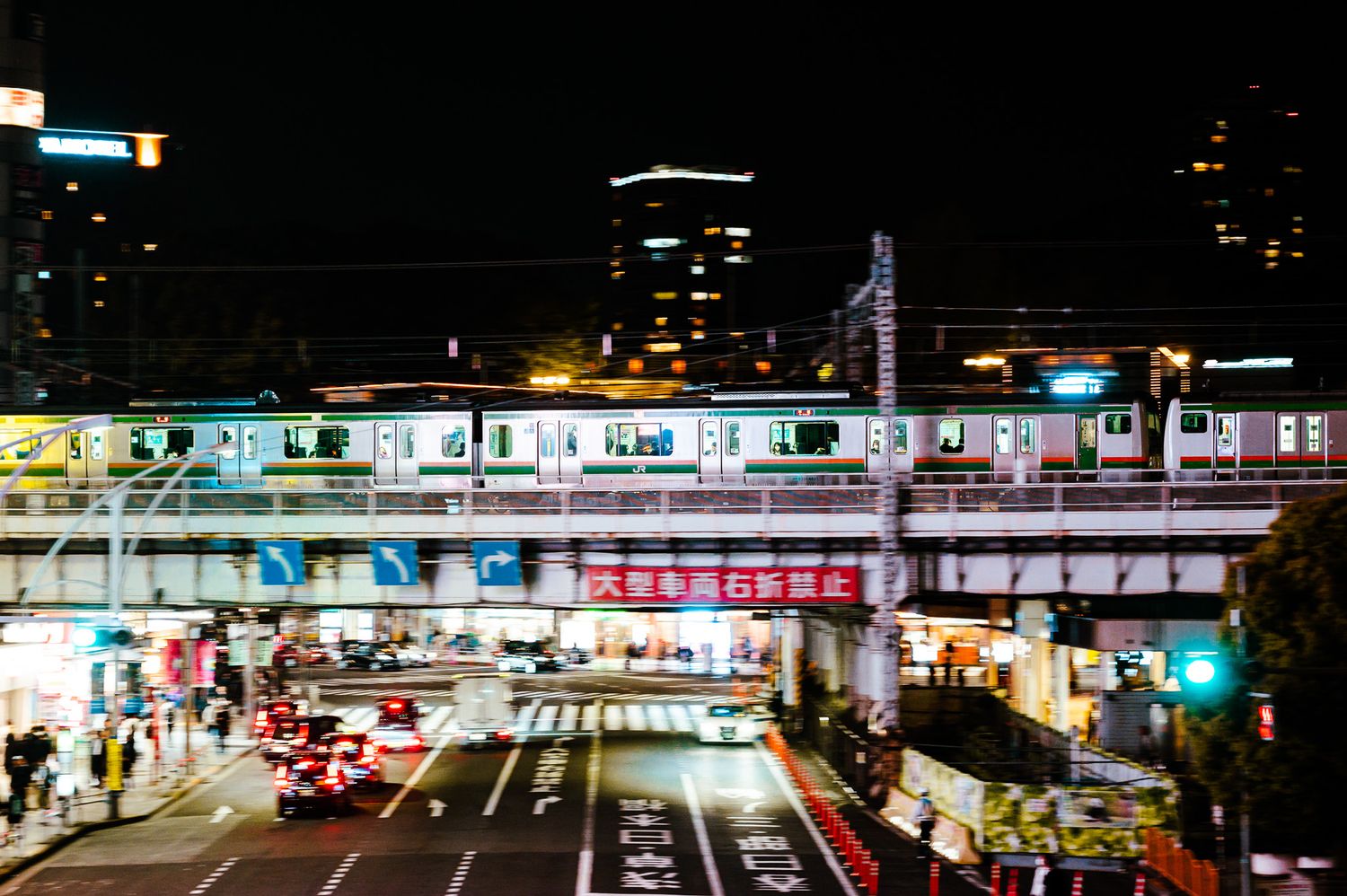 Elevated train tracks over a busy Japanese street illuminated by city lights at night.