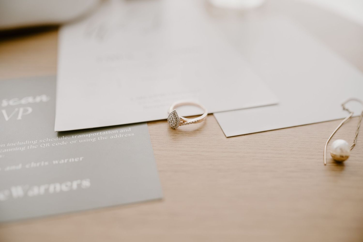 Close-up of wedding rings and pearl jewelry on minimalist invitation cards.