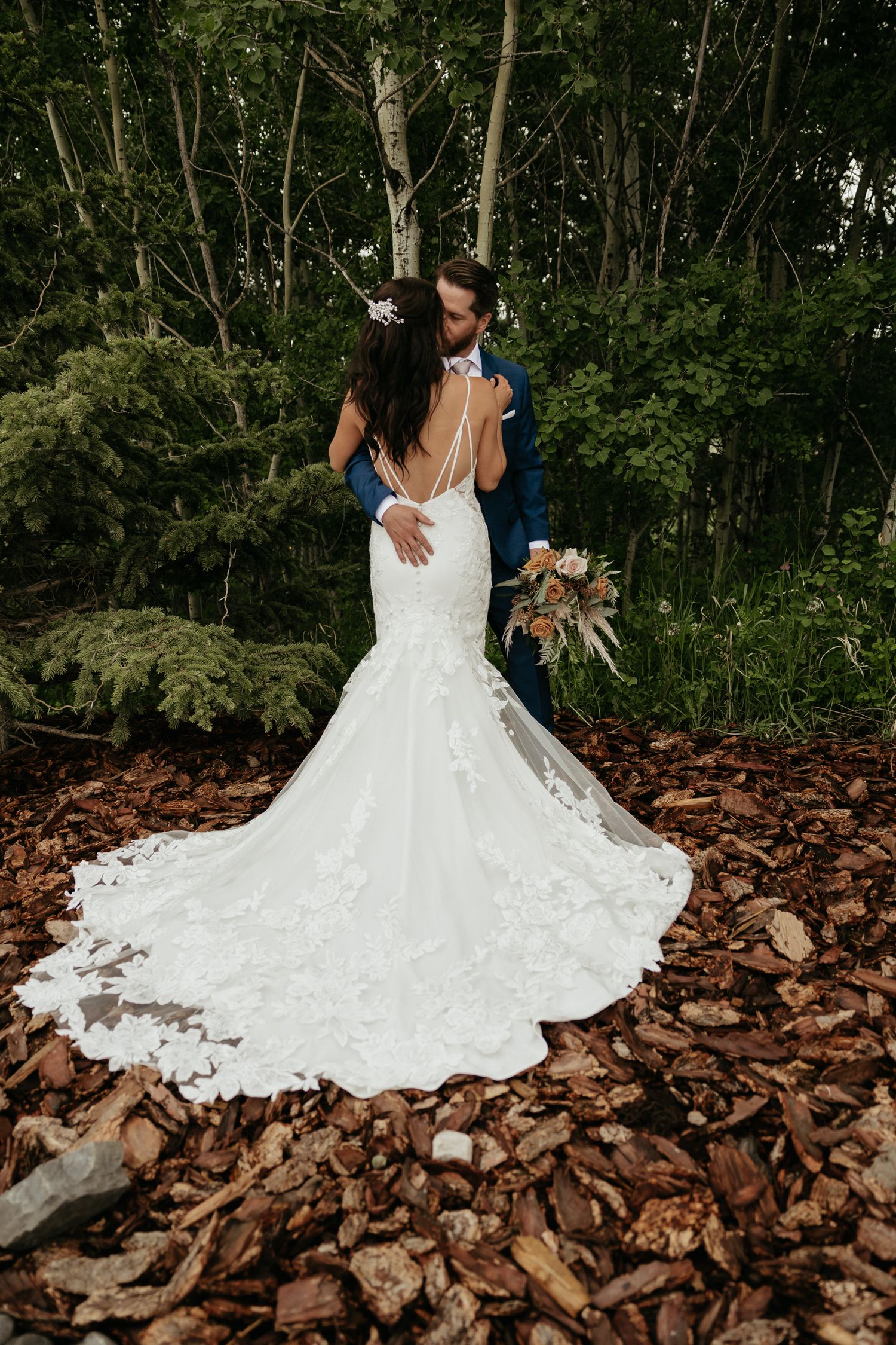 Beautiful white wedding dress train spread out on rustic rocks in a forest setting.