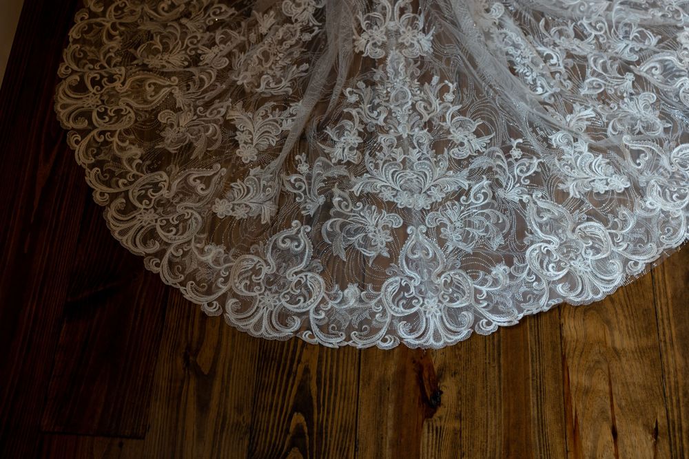 Intricate lace detail of wedding dress train spread out on wooden floor.