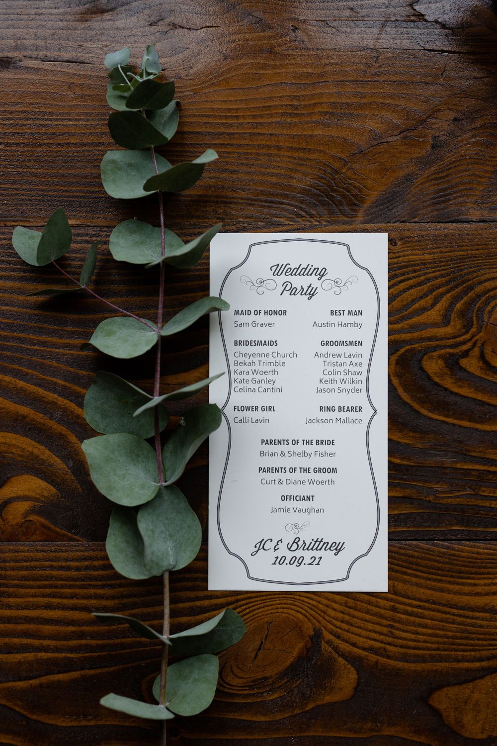 Wedding party program card decorated with eucalyptus leaves on dark wooden background.