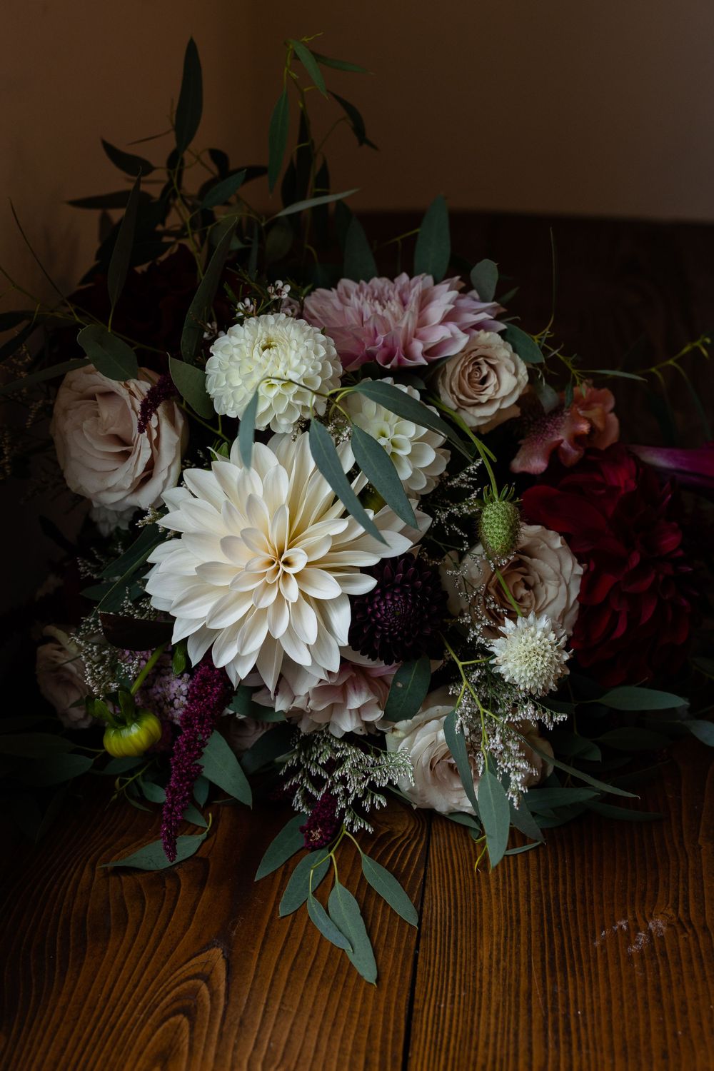 Elegant wedding bouquet with dahlias, roses, and mixed flowers in white, pink and burgundy tones.