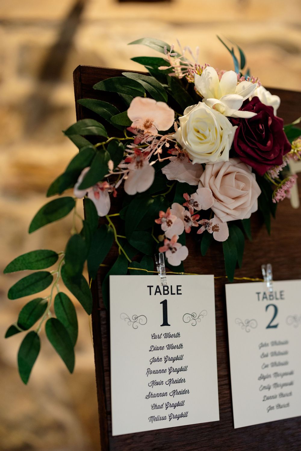 Wedding table assignment cards numbered 1 and 2 with floral arrangement of roses and greenery.