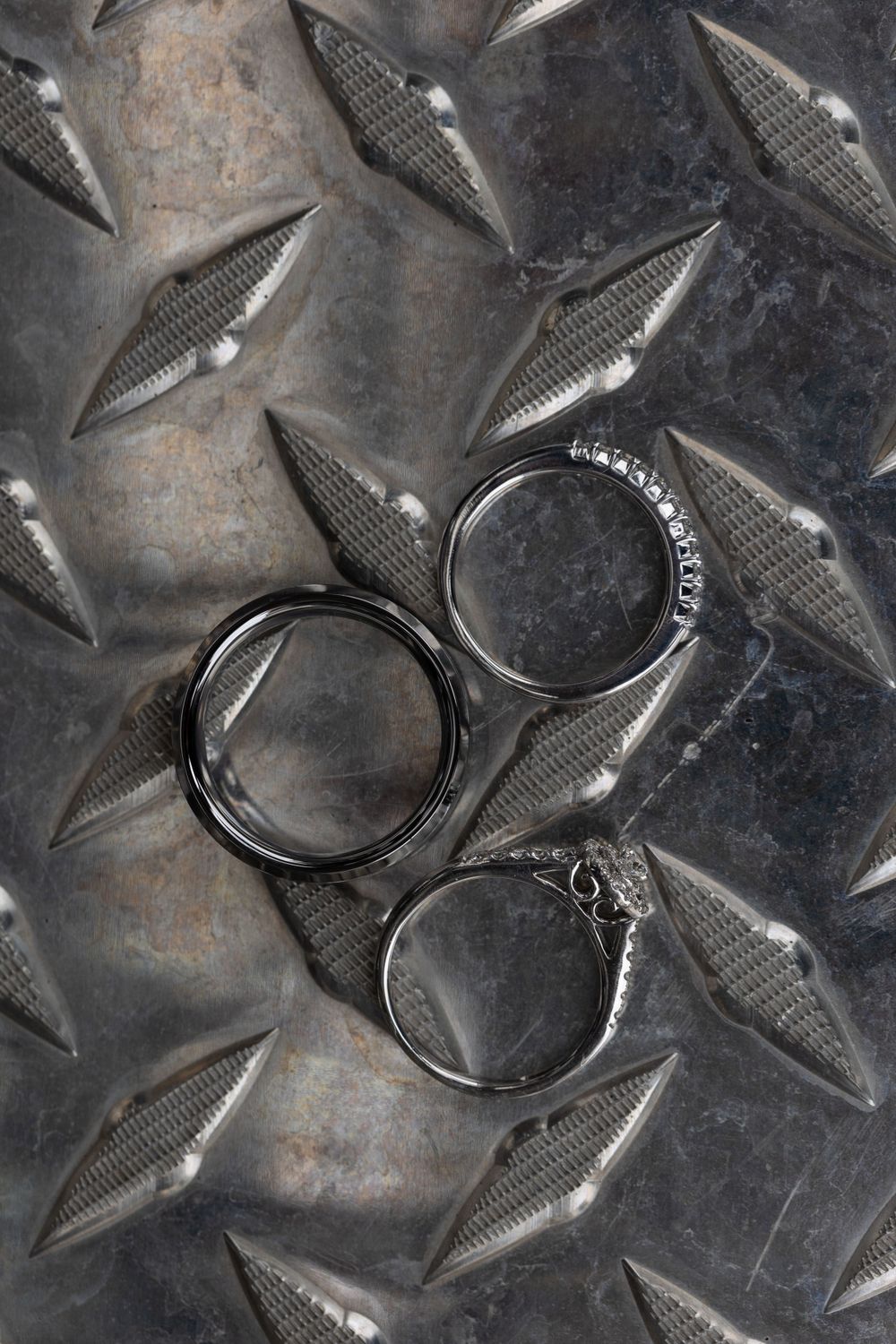 Three wedding bands arranged on a textured metal diamond plate background.