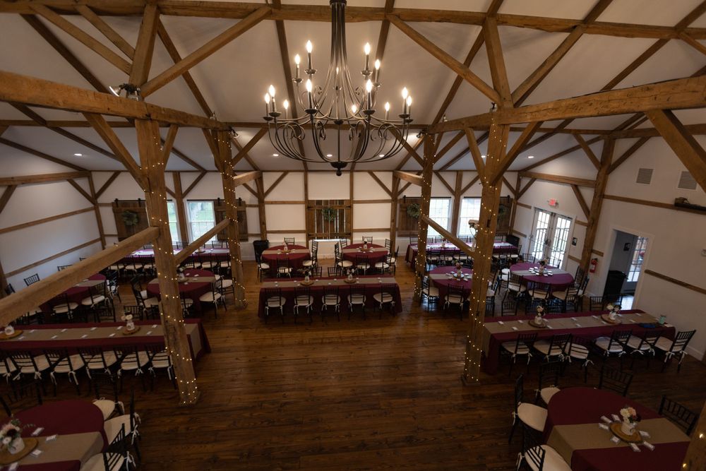Large rustic reception hall with wooden beams and chandelier set up for an event.