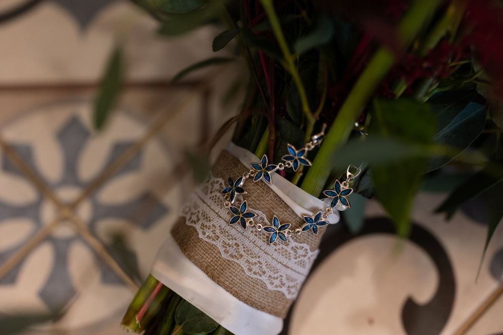 Wedding rings adorned with blue gems displayed on lace against a patterned tile background.