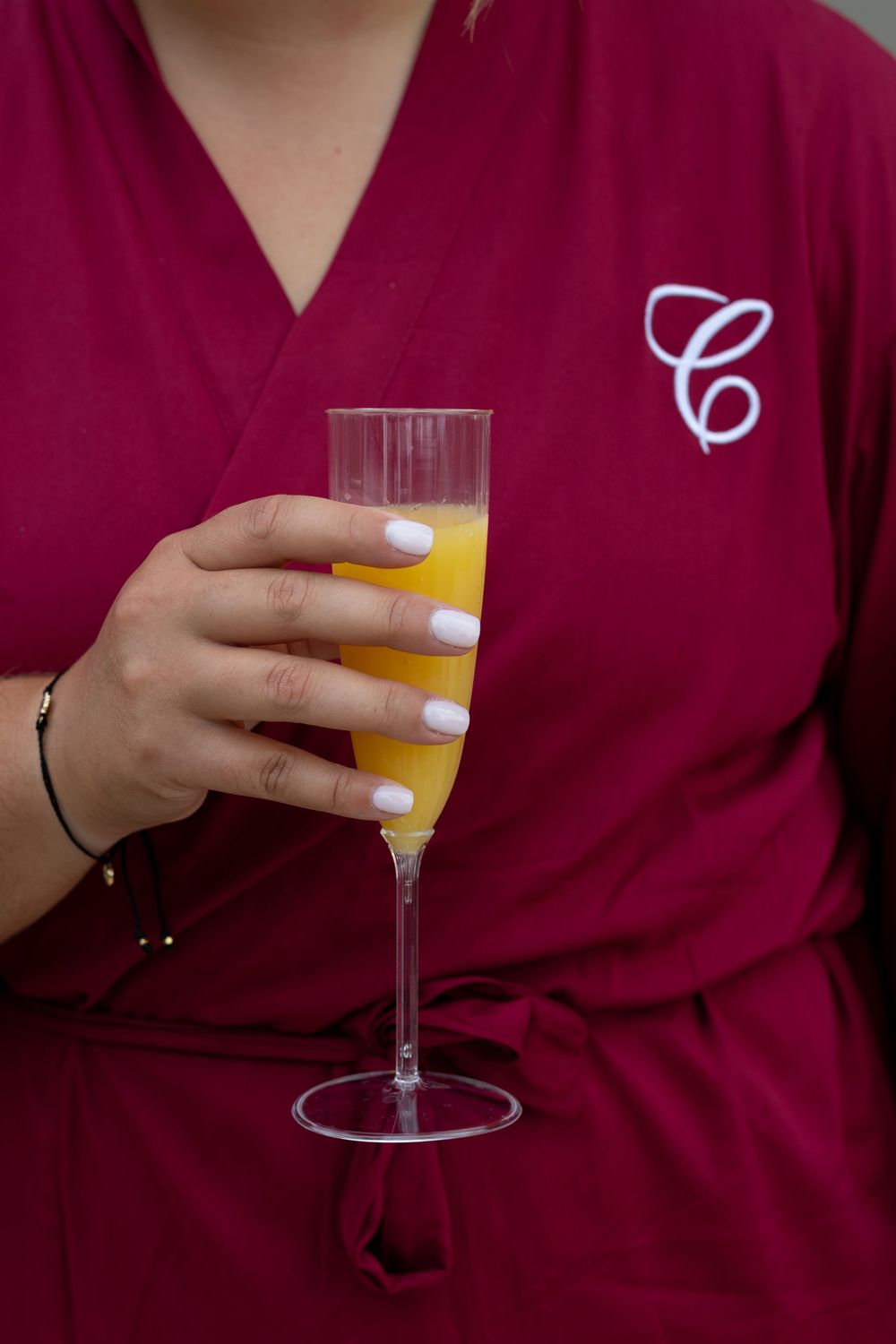 Hand holding a mimosa glass while wearing a burgundy monogrammed robe.