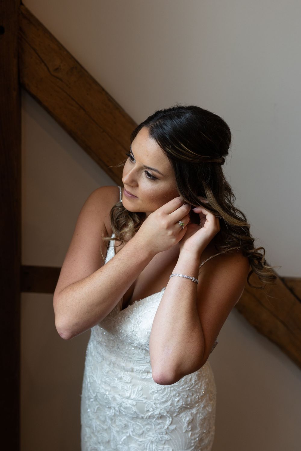 Person in white lace dress adjusts earrings while getting ready.