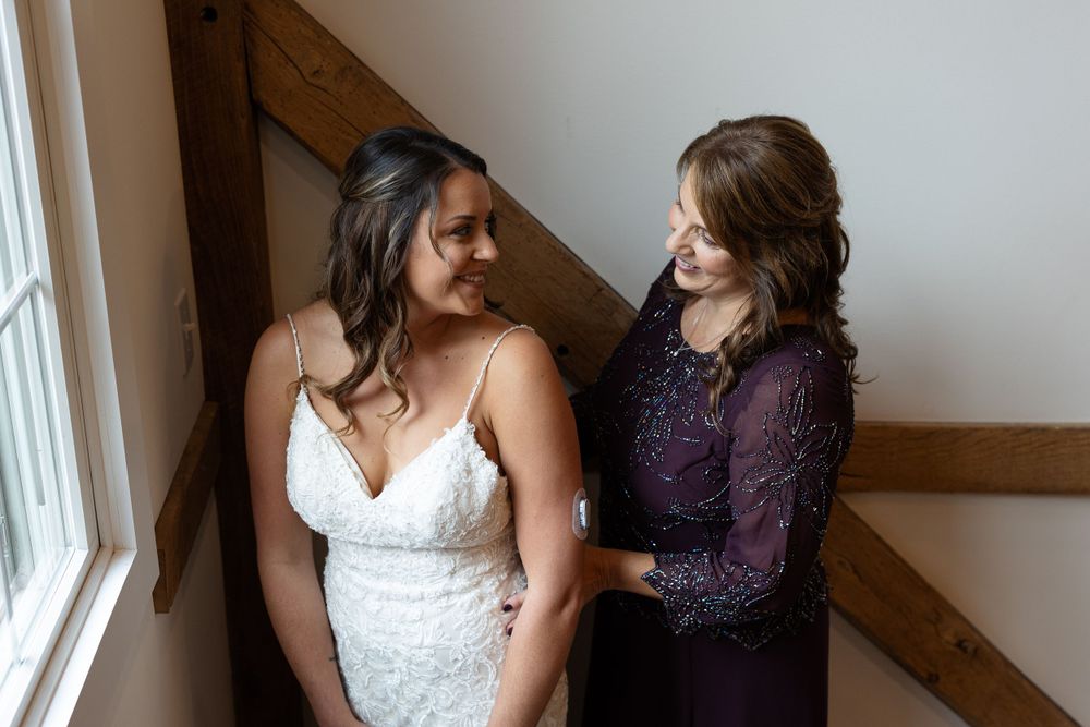Two women share an intimate moment by a window, one in a white wedding dress and another in purple.