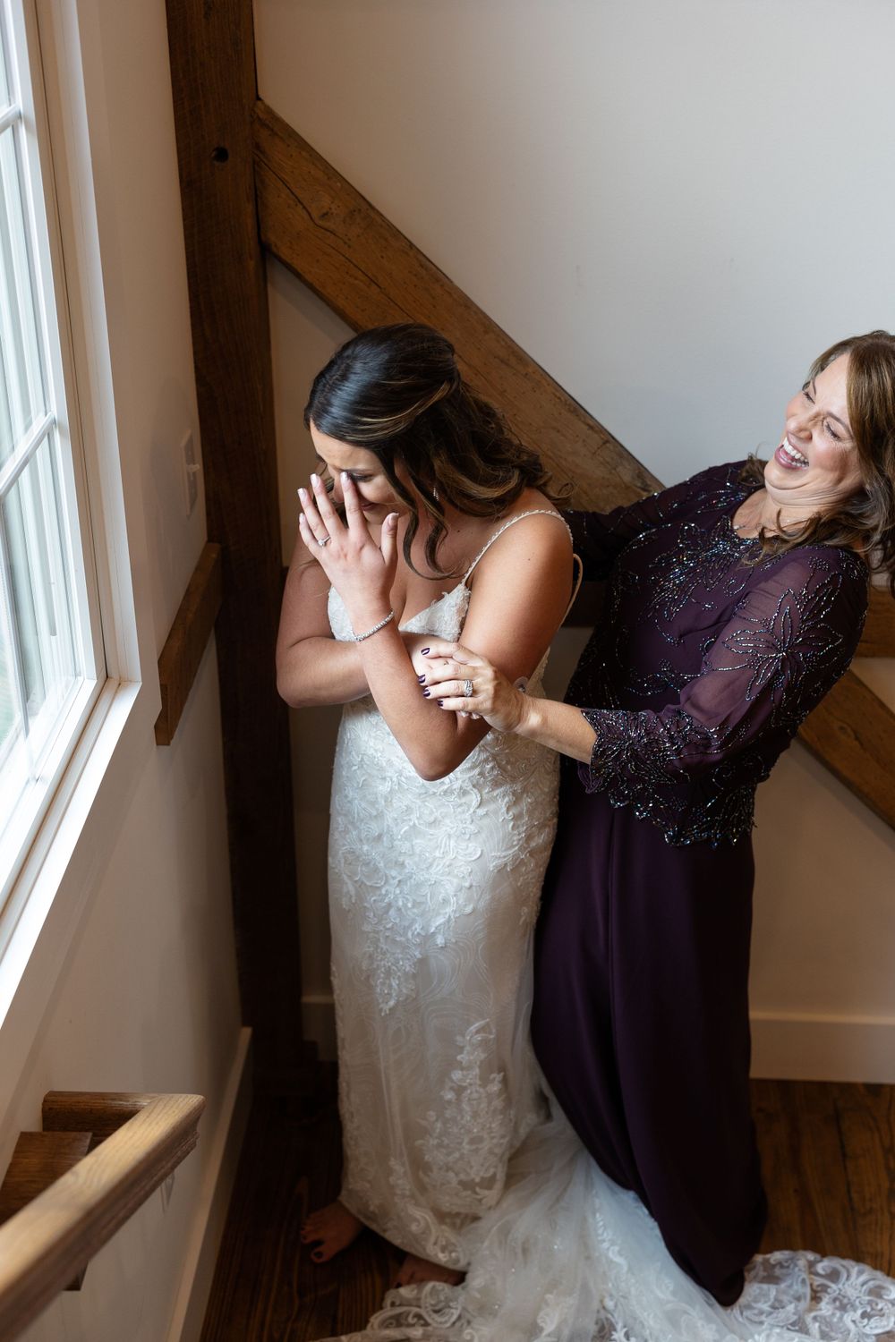 Emotional wedding moment captured between two women by a window in a rustic setting.