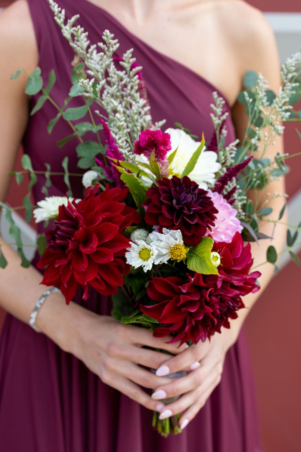 Burgundy and white floral bouquet with dahlias and greenery held by person in purple dress.