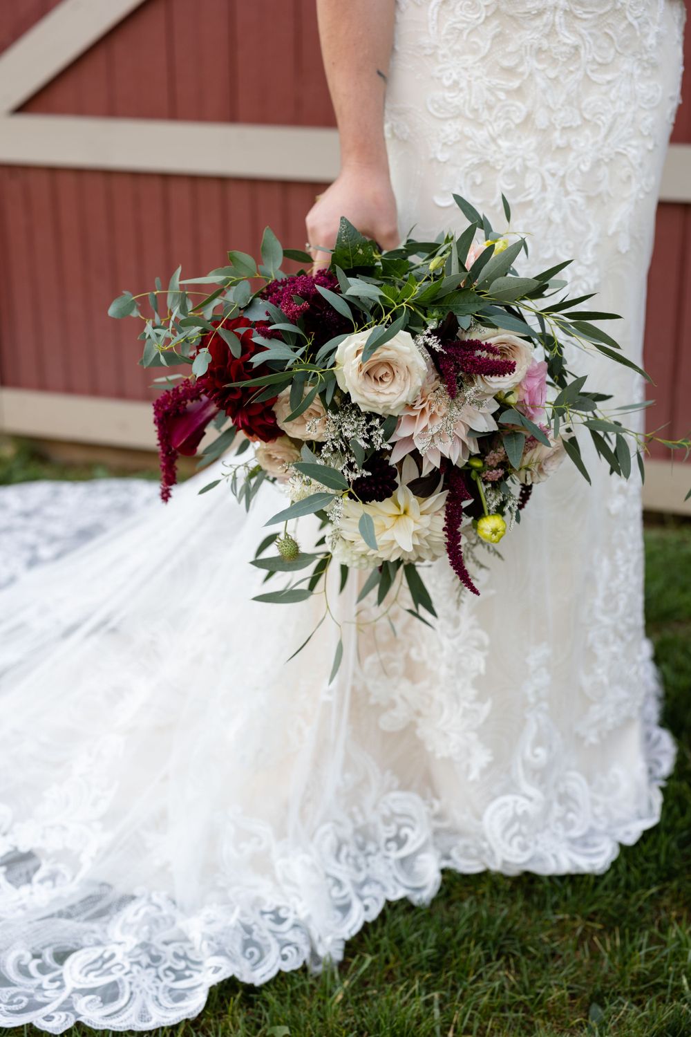 Wedding bouquet with burgundy and white flowers against lace dress train.