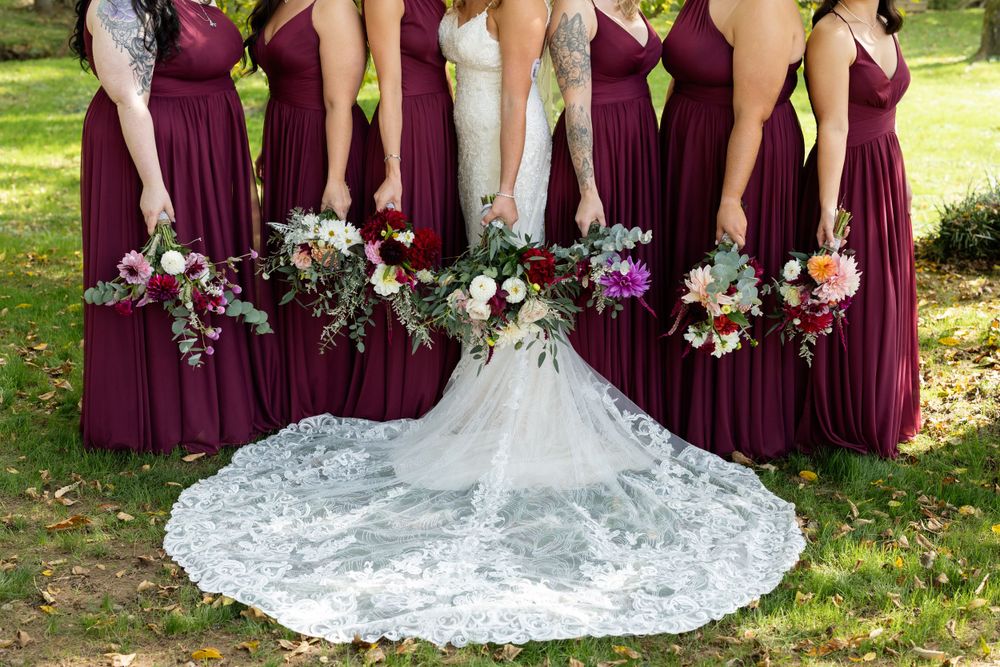 Bridal party shows off their gowns and bouquets in playful pose with bride's lace train displayed.