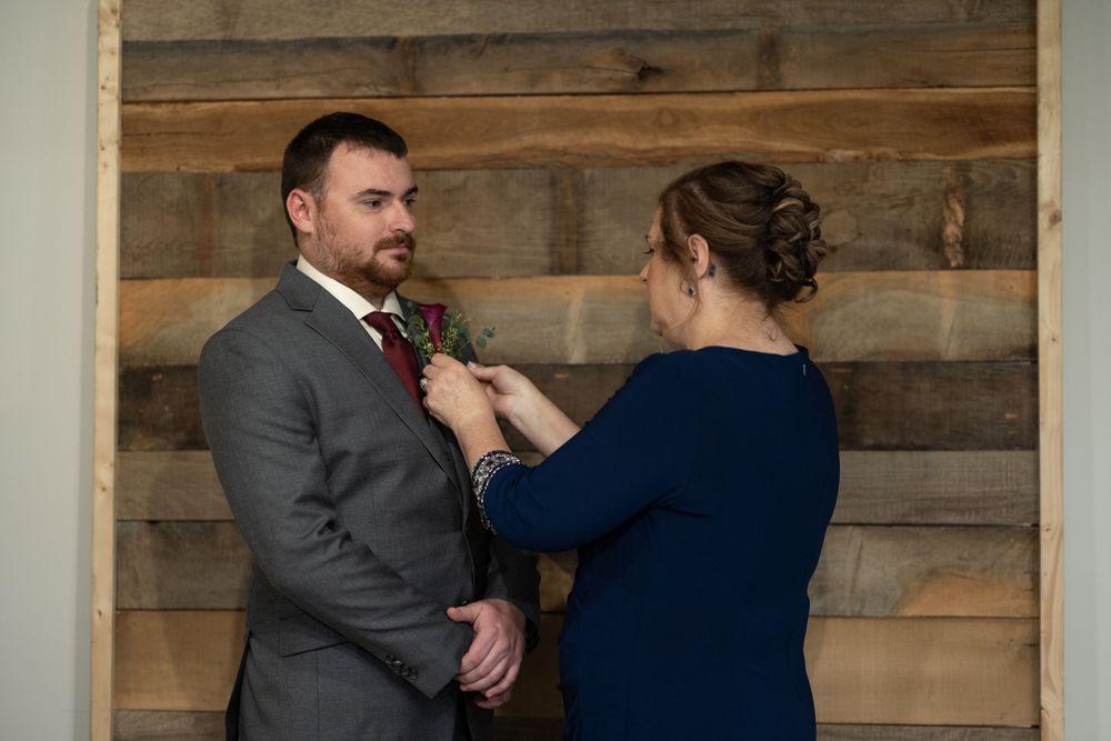 Final boutonniere adjustments being made against rustic wooden wall background.