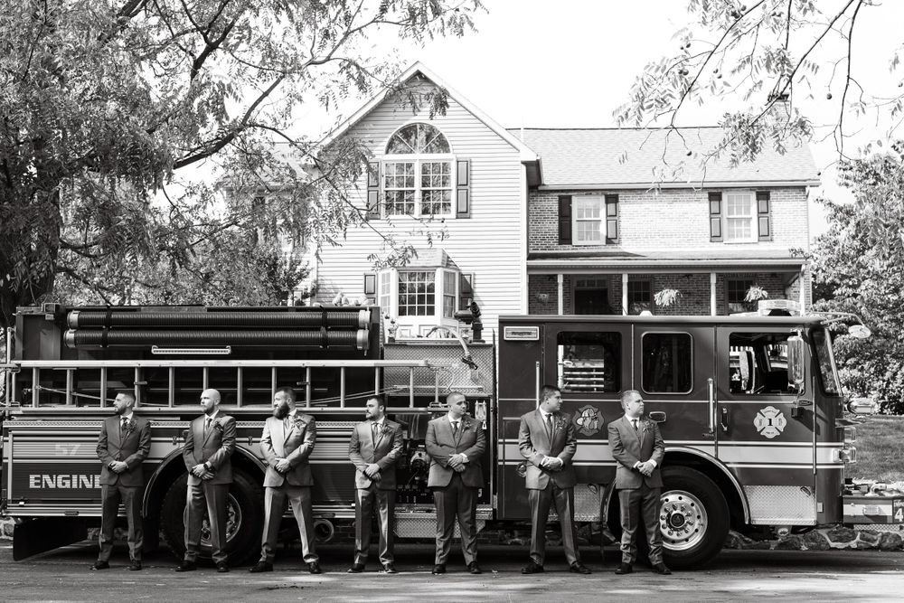 Black and white photograph of a wedding party posing with a vintage fire truck.