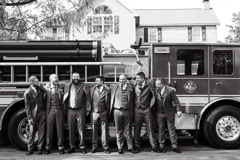 Monochrome image of wedding attendees lined up against a vintage fire engine.