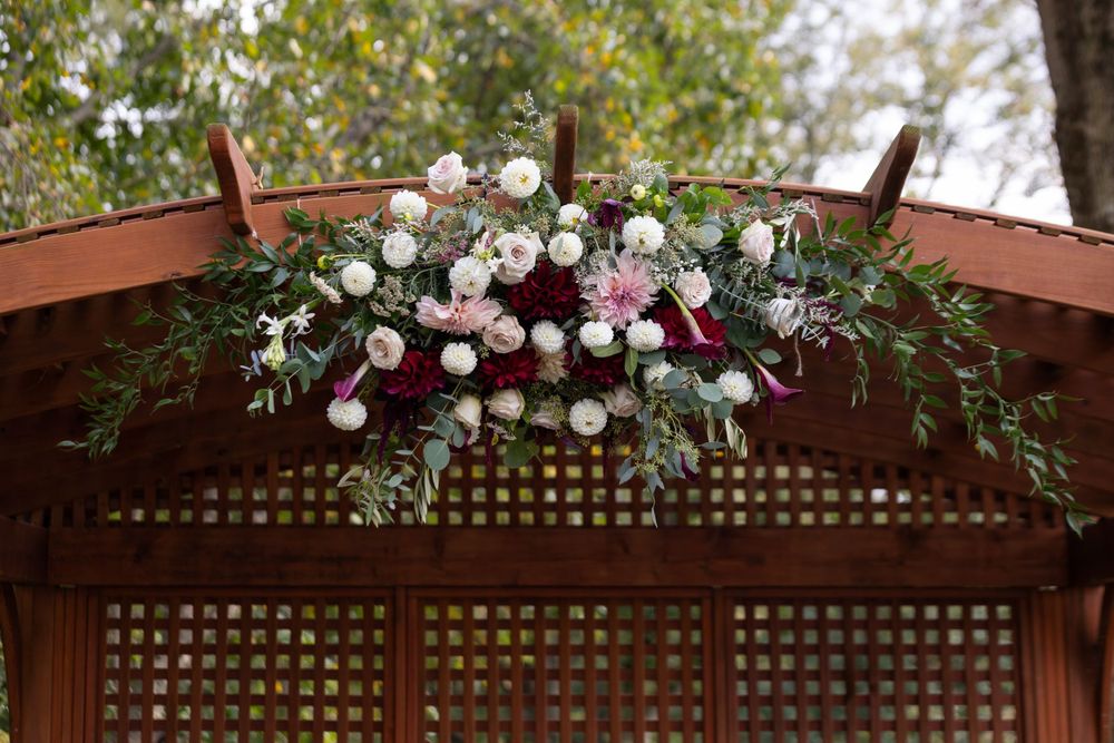 Elegant floral arch decoration with white and burgundy flowers against wooden lattice.