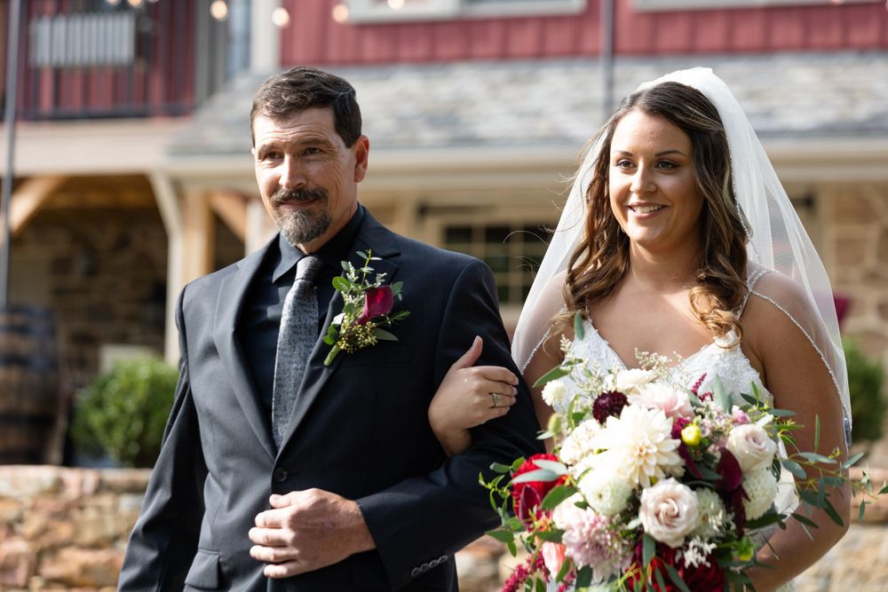 Outdoor wedding ceremony at rustic barn venue with floral bouquet.