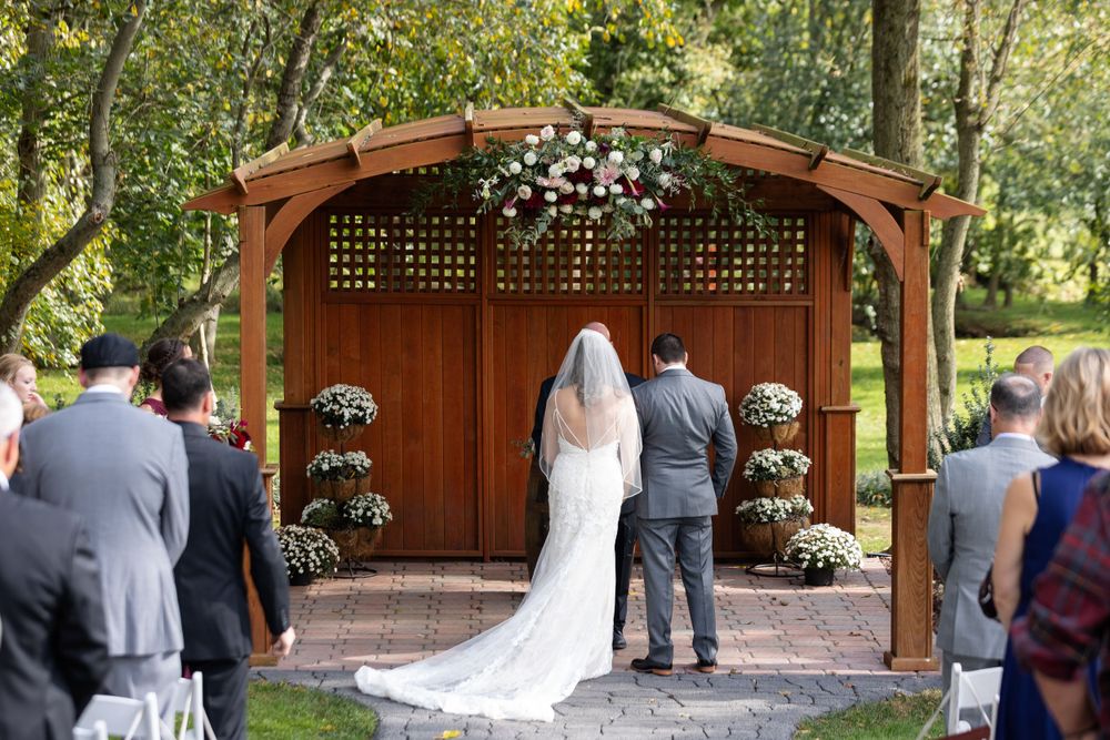 Wedding ceremony under wooden gazebo decorated with white flowers.