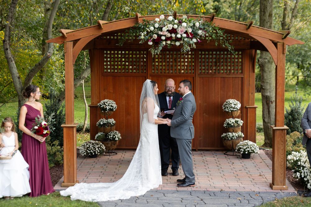 Outdoor wedding ceremony in wooden gazebo adorned with white flowers and greenery.
