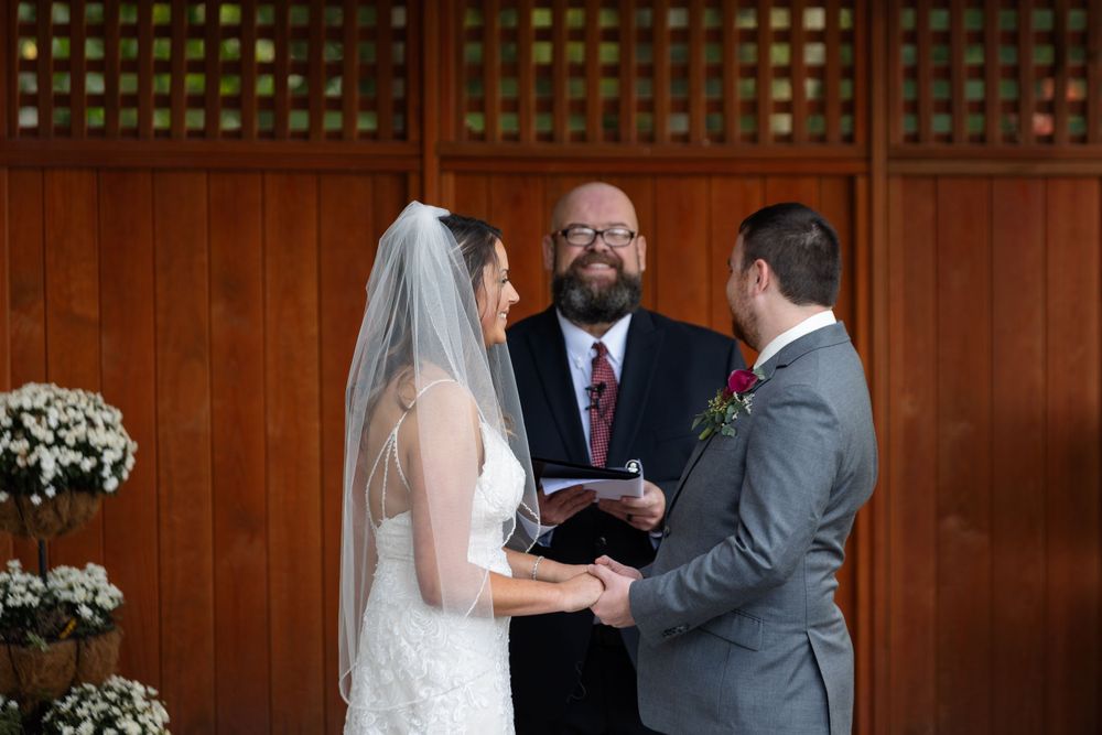 Intimate wedding ceremony moment under rustic wooden pergola with floral decorations.
