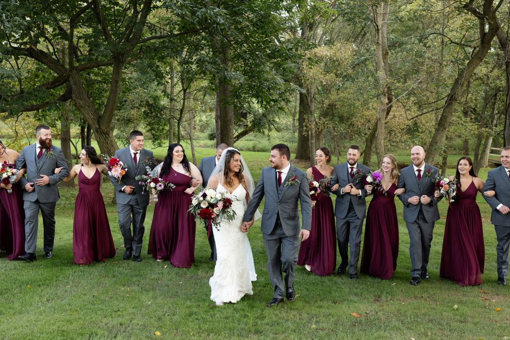 Wedding party poses together on lawn with bridesmaids in burgundy gowns and groomsmen in gray suits.
