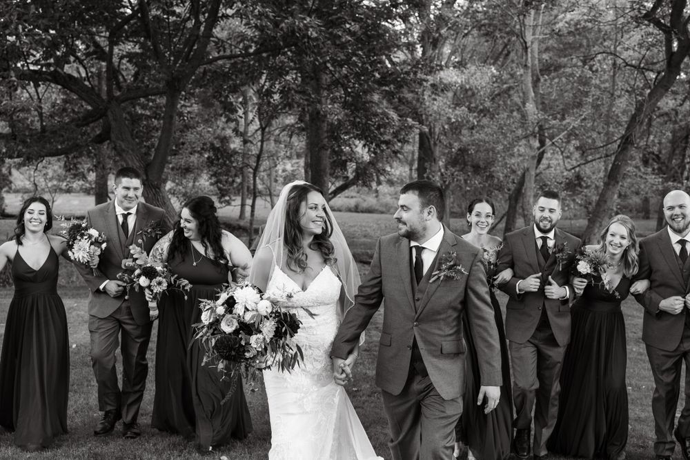 Black and white photo of wedding party walking and laughing together outdoors.