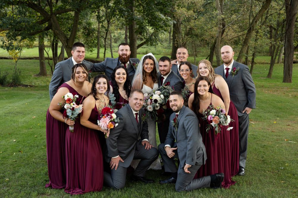Wedding party poses for casual group photo on grass with burgundy and gray attire.