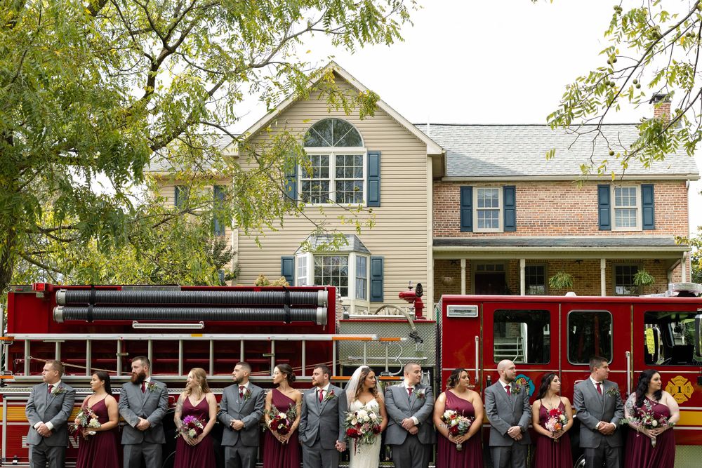Wedding party poses in front of vintage red trolley and classic house.