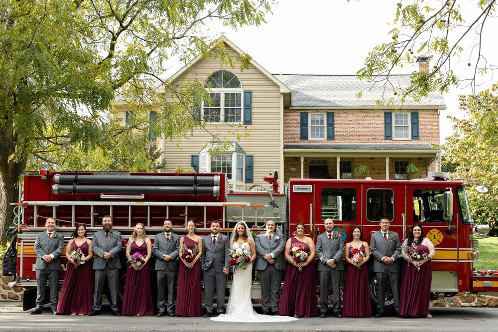 Wedding party lines up alongside red trolley car in front of traditional two-story home.